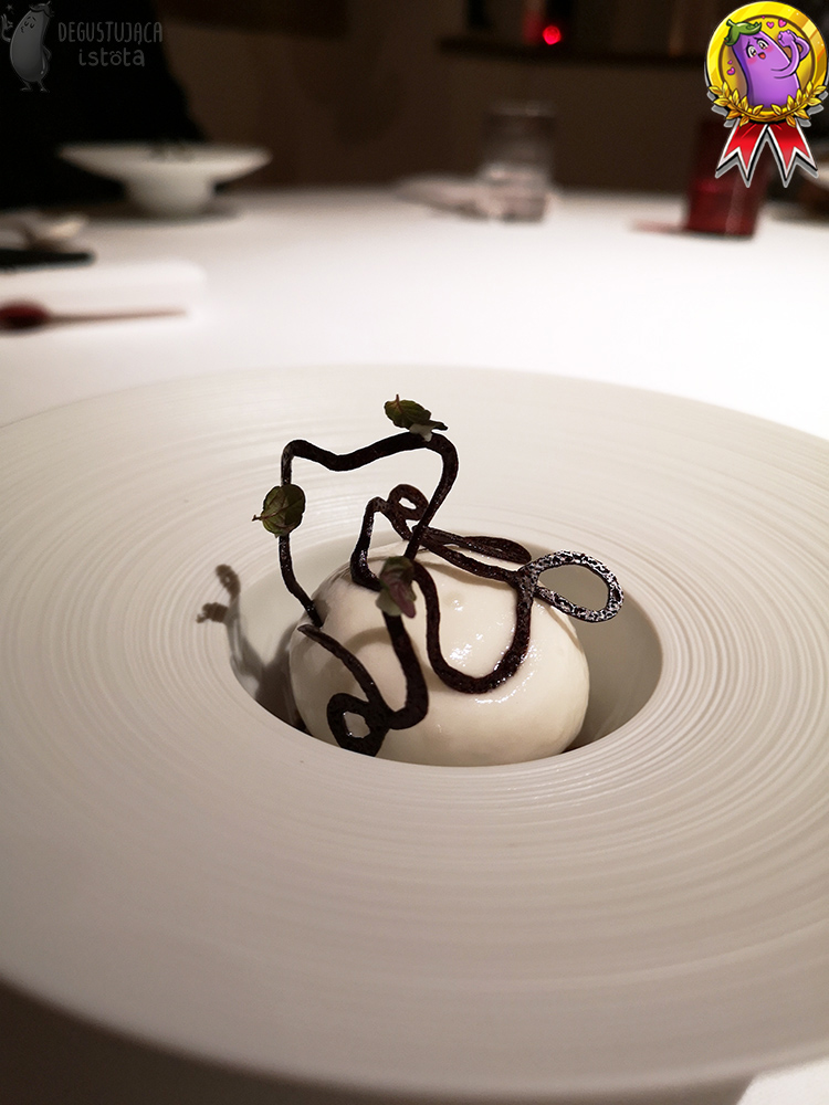 In a white deep plate is a ball of white foam. On top of the foam is a chocolate snake with dark leaves glued to it.