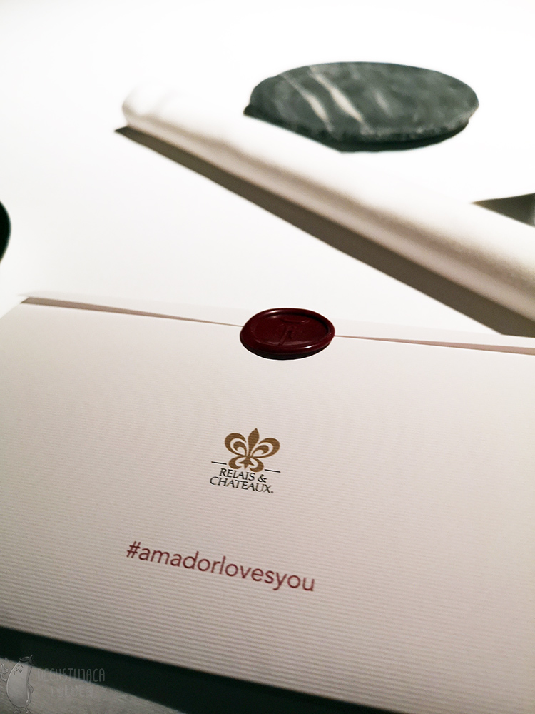 Photo of a sealed white envelope with red lettering/hashtag amador loves you and the Rails and Chateaux logo.