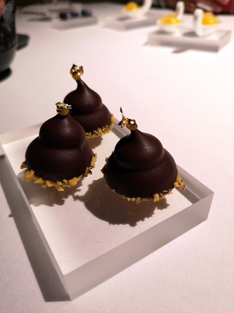  Chocolate forms in the shape of gnome hats with gold pompoms are placed on a transparent coaster.