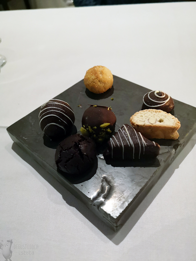 Chocolate pralines and cookies are arranged on a black rectangular stone.