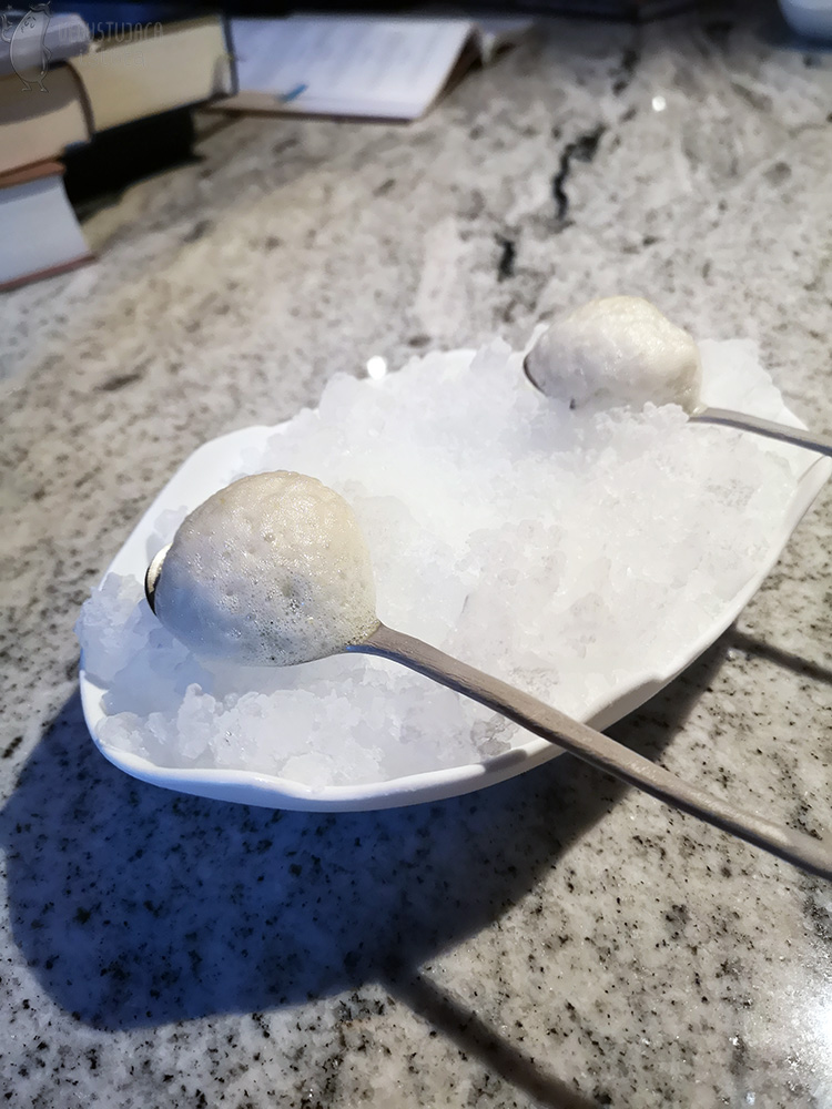 In a white bowl, two teaspoons filled with frozen white foam.