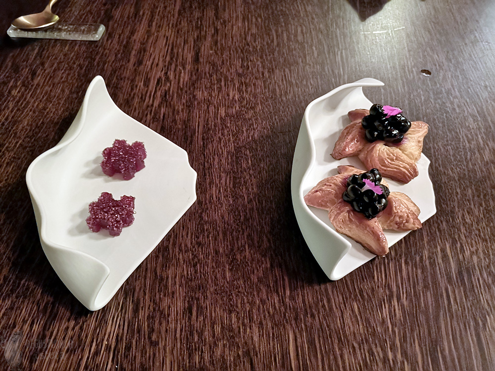 Two small saucers. One with two blueberry danish pastries, the other with two pink flower-shaped sugar jellies.