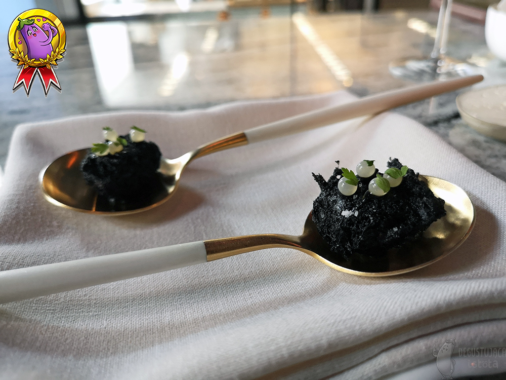 Na złotobiałych łyżeczkach leżą ślimaki w czarnej tempurze, udekorowany białymi kuleczkami kawioru.