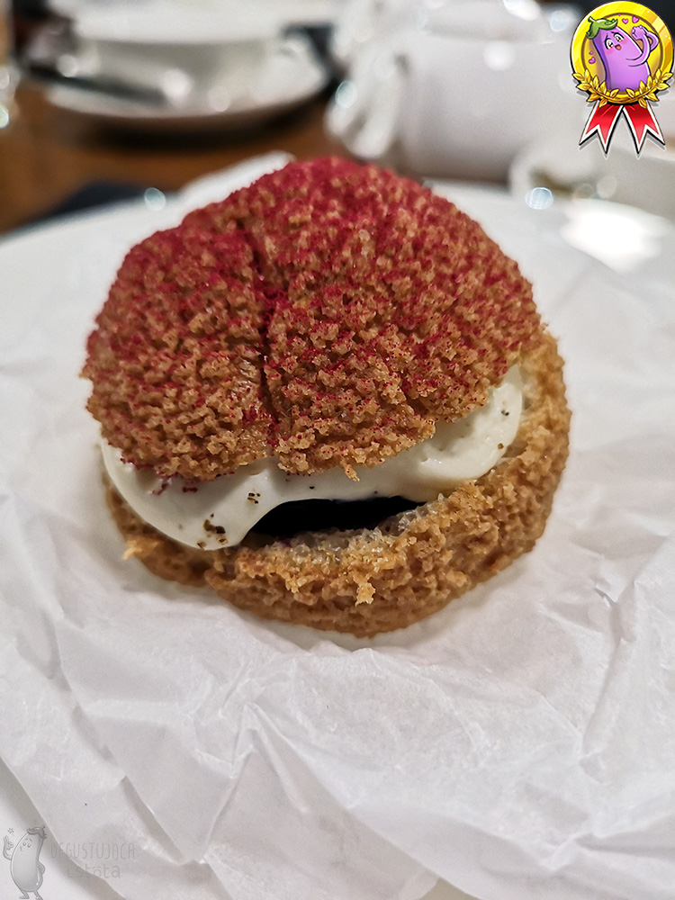 A large, white, flat plate with a puff in the center. The puff lies on rolled up baking paper. The top is sprinkled with red powdered sugar.