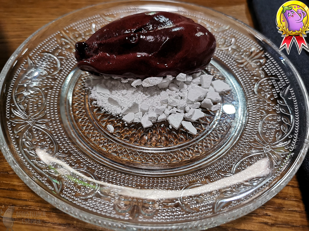 Na przezroczystym talerzu leżą fioletowo czerwone lody na pokruszonej białej bezie