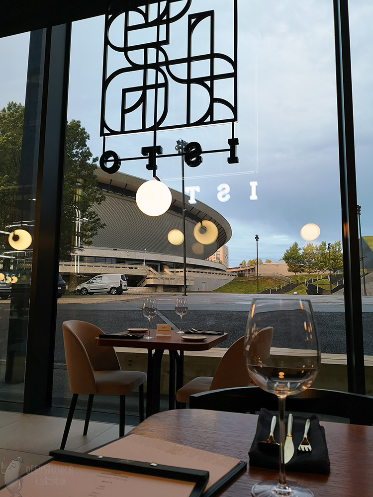 You can see part of the Spodek through the windows of the restaurant with the Isto logo. The sky is overcast and the evening is coming.