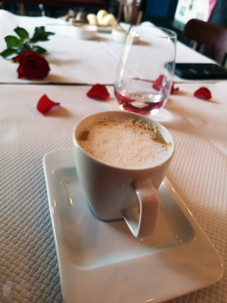 Coffee in a white cup on a rectangular saucer. A red rose in the background.