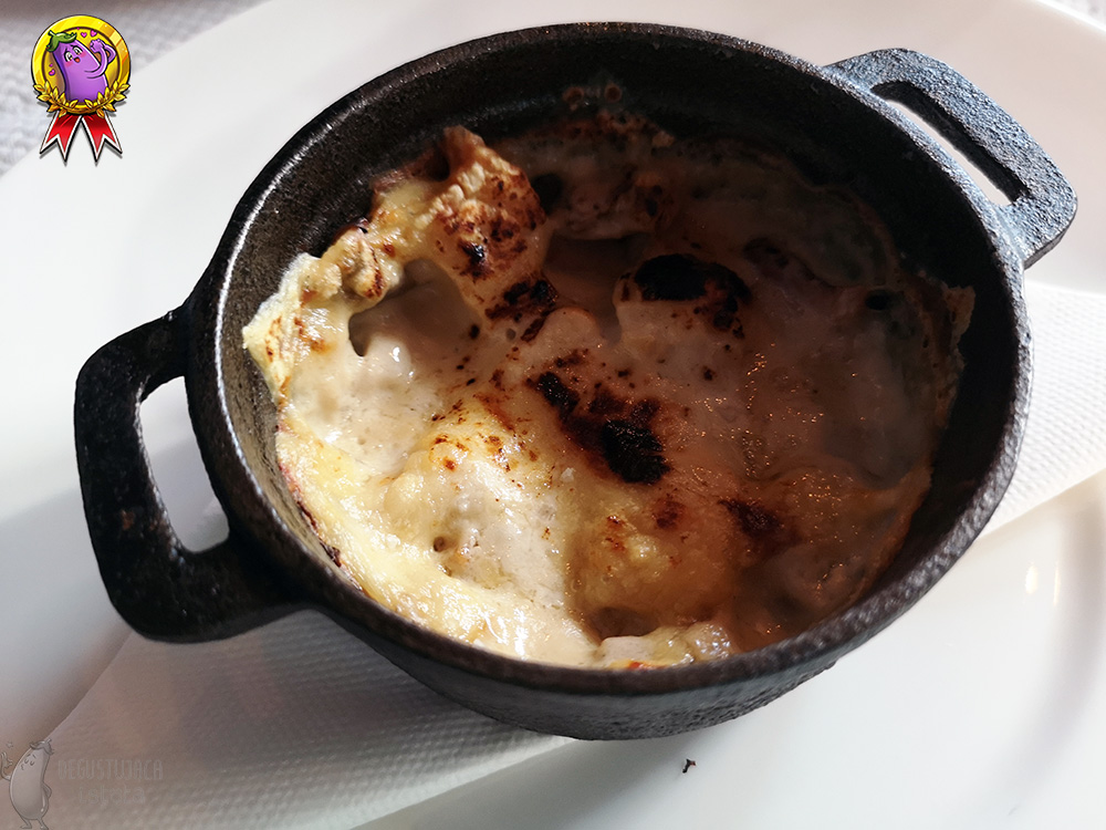 A small, black, cast iron casserole pot, which is covered on top with a browned layer of cheese.