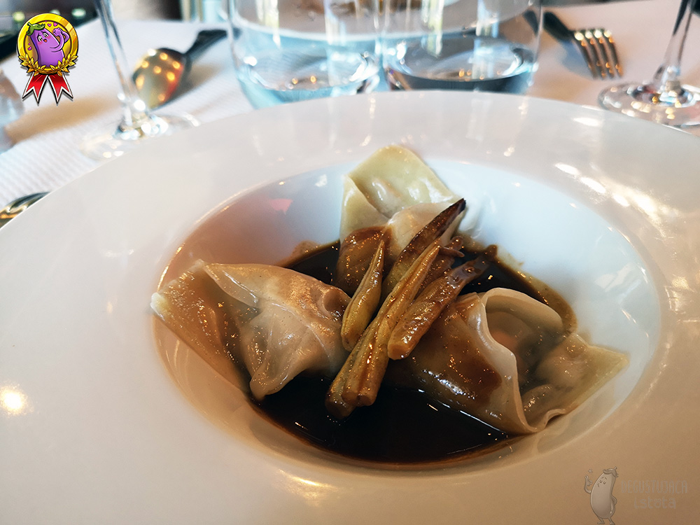 In a white deep plate with a wide, In a white deep plate with a wide flat rim, three dumplings are placed and covered with a dark sauce. In the middle between the ravioli are yellow beans, also covered with sauce.