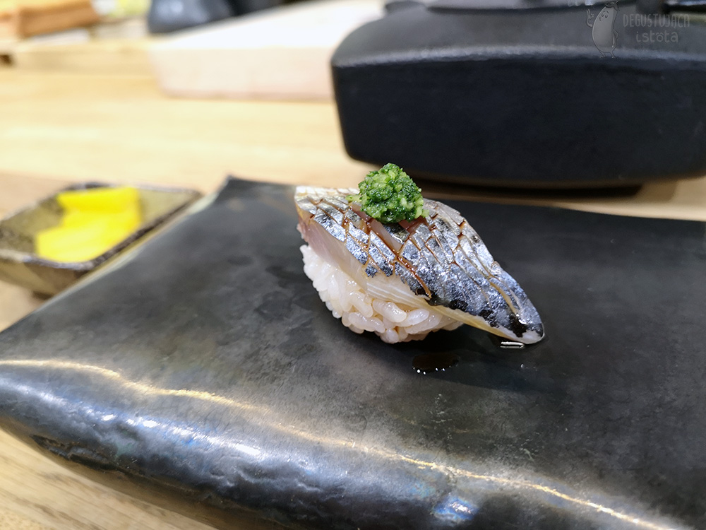 Nigiri z kawałkiem makreli ze skórą, ponacinaną drobno i porcją zielonej mieszanki imbiru i dymki na górze.