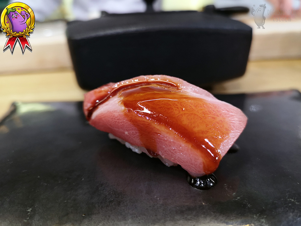 A large piece of tuna meat, pink with clear marbling smeared with a thick plum sauce. A bit of rice is visible from underneath.