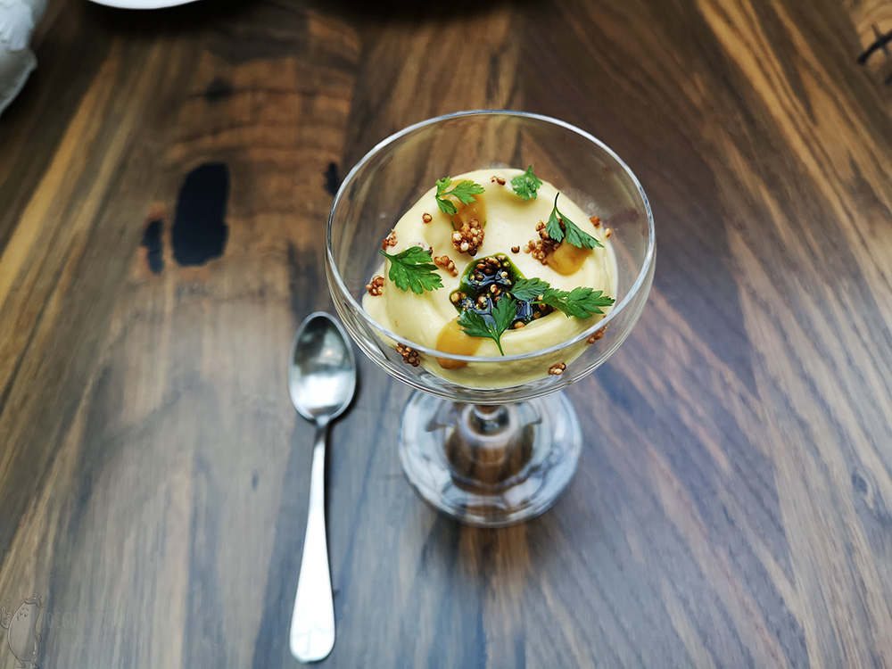 In the glass is an orange portion of sorbet with chunks of amaranth crisps and green chervil oil.