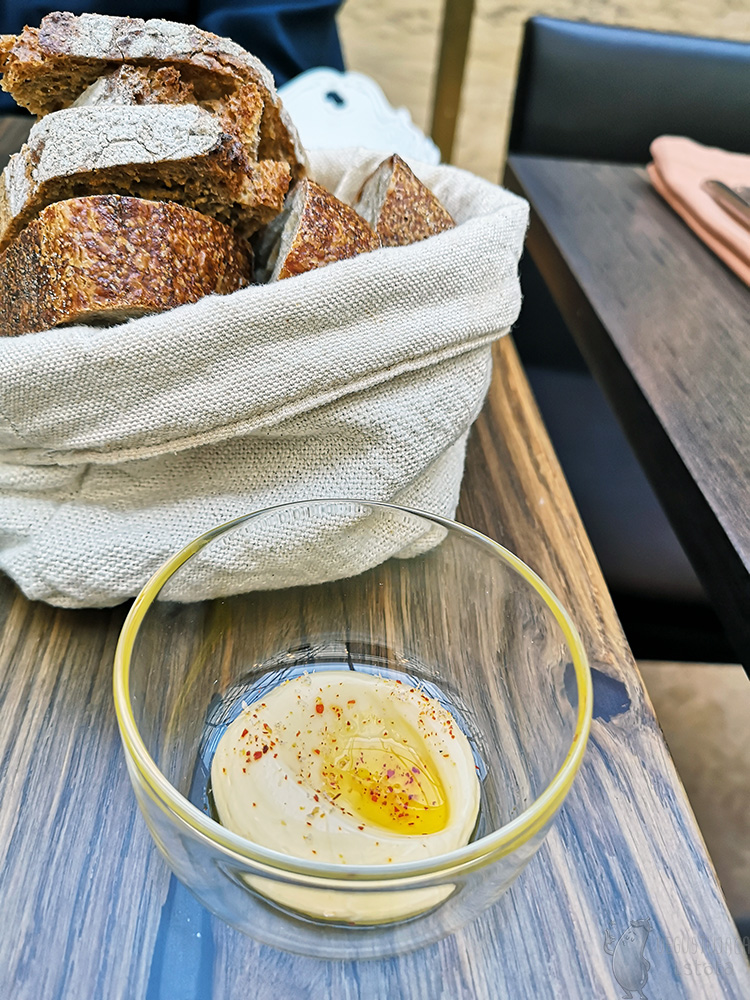 A small glass bowl of butter sprinkled with paprika and topped with oil, a basket bag of bread.