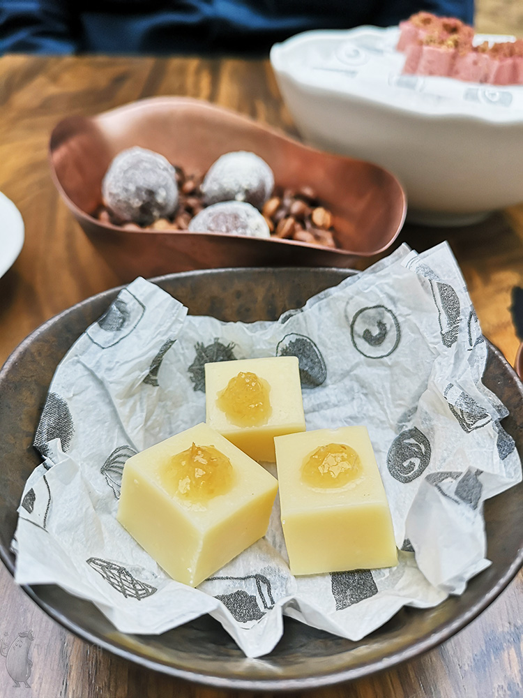 In a metal bowl are three cubes of white chocolate with yellow jam on top.