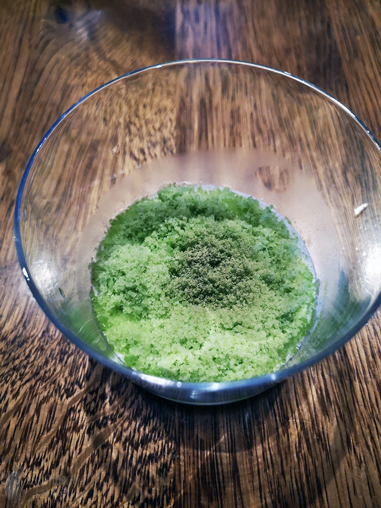 Wnętrze małej szklanki z zieloną warstwą pudru, która przykrywa białą panna cottę.