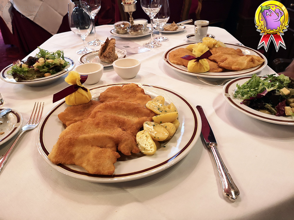 On a table with a white tablecloth are two large, flat plates with schnitzels and two deep plates with salads.