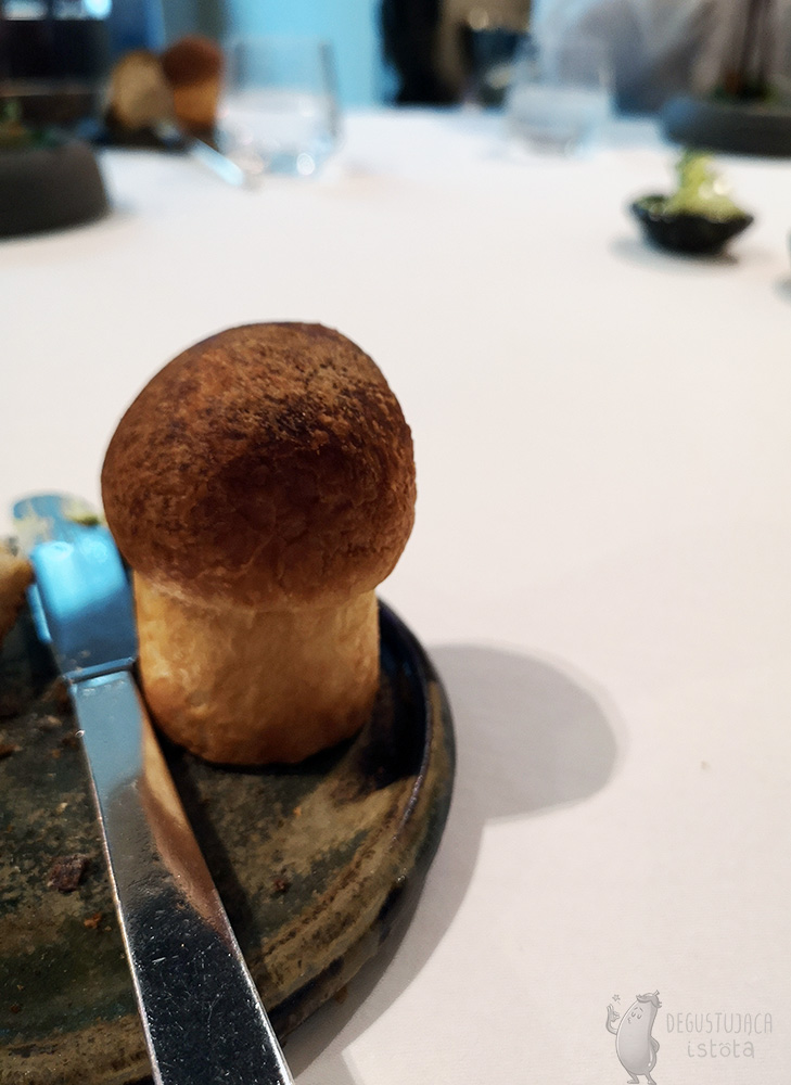 On the edge of the grey-green plate there is a mushroom-shaped brioche.