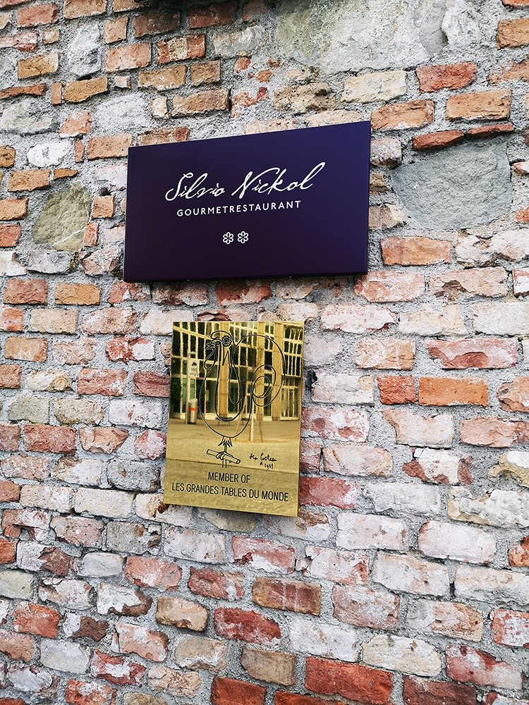 On the red brick wall, in front of the entrance to the The Palais Coburg is a violet Michelin Guide starboard and a gold plate with information about it, that the restaurant is in the guide Les Grandes Tables du Monde.
