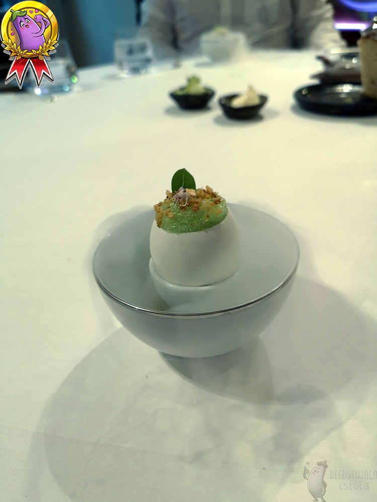 Jajko z zieloną pianką, umieszczone w połówce ceramicznego jajka z którego unosi się para.