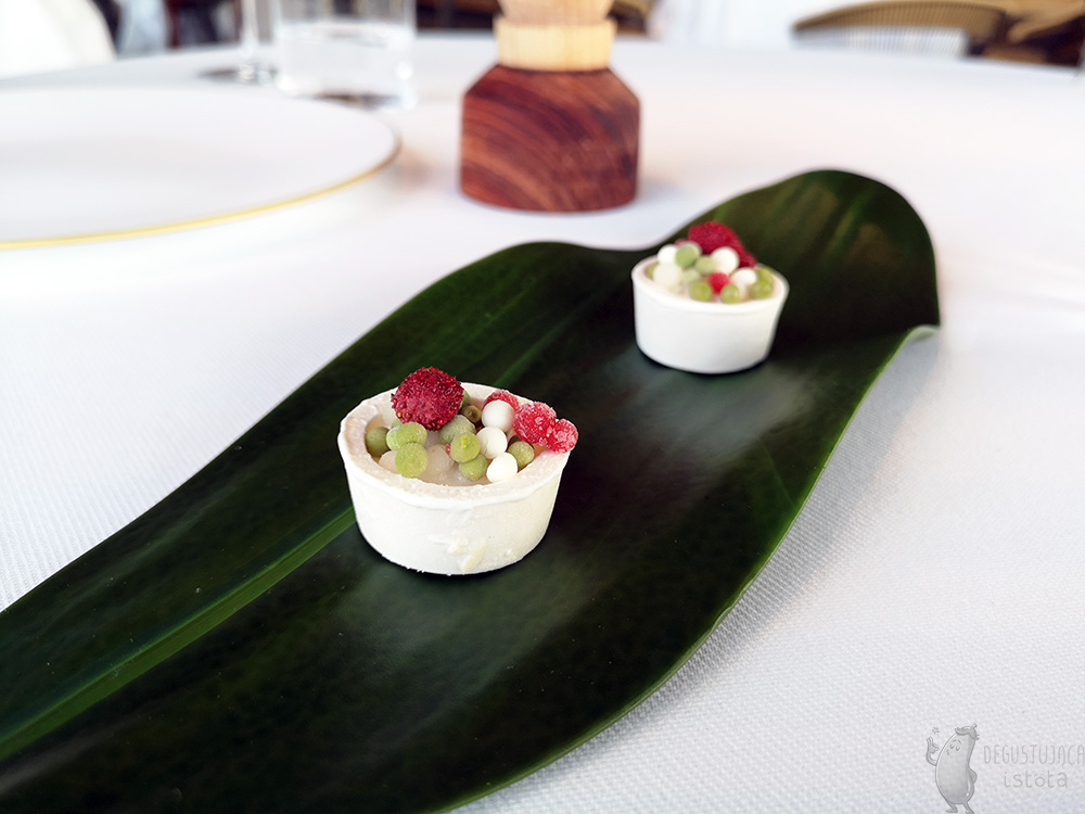 Na talerzyku w kształcie liścia leżą dwie lekko różowe tartaletki wypełnione kuleczkami w kolorach: zielonym, różowym i białym.