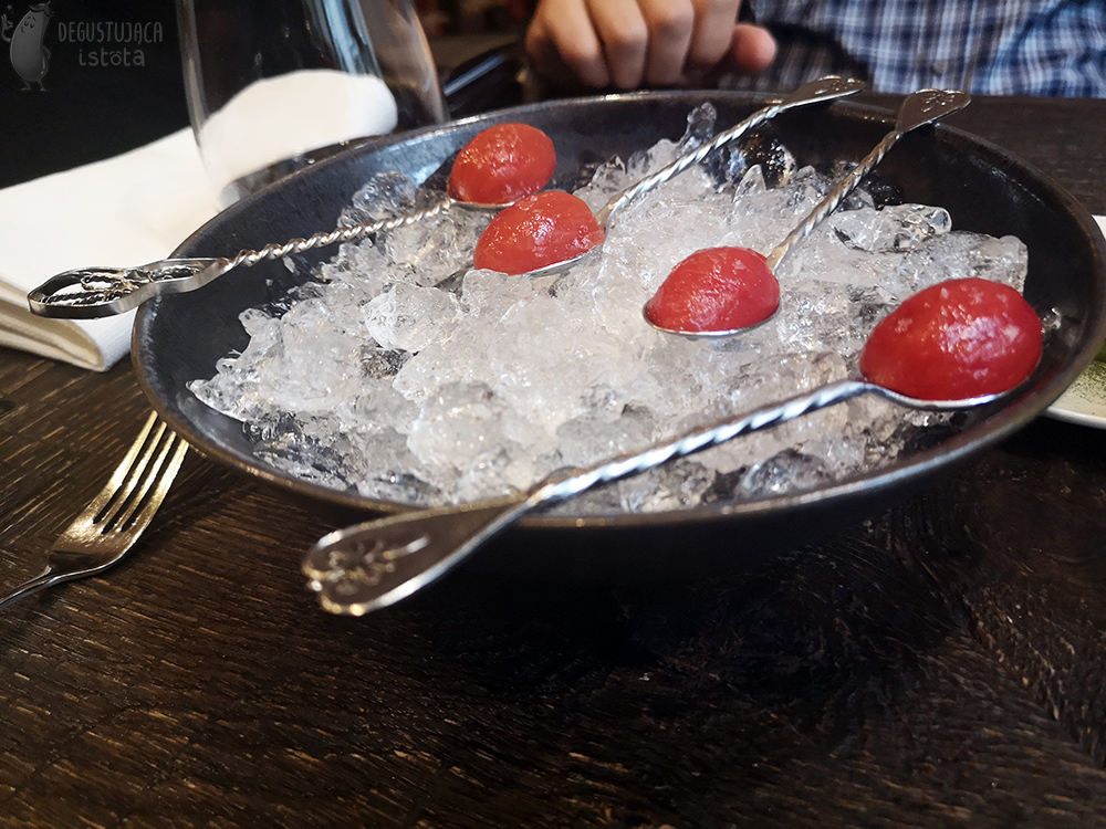Miska z lodem na którym leżą małe pomidorki bez skórki na srebrnych łyżeczkach.