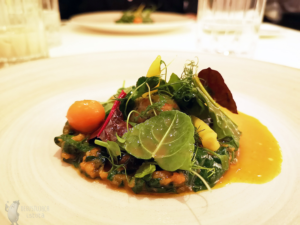 Small carrots and spinach leaves arranged on a white plate. Poured with orange sauce.