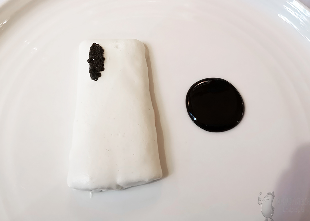 Filet węgorza pokryty białą pianką. Na niego nałożony w jednym rogu czarny kawior. Obok kółko z sosu z czarnego bzu