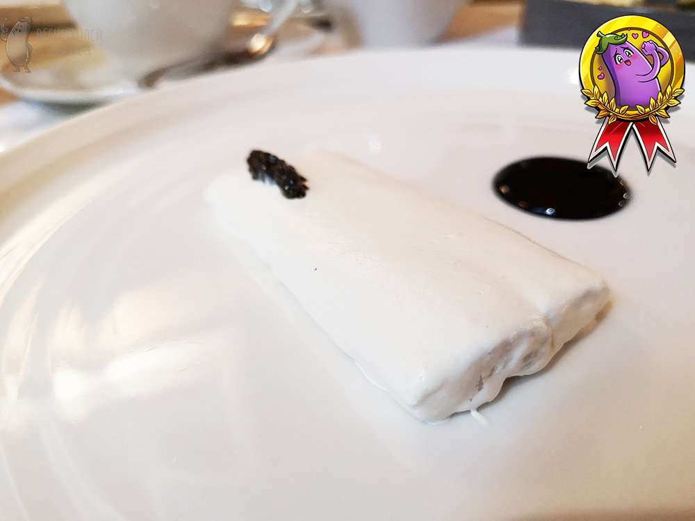 Eel fillet surrounded by horseradish foam with a bit of black caviar. Next to it is a circle of black elderberry sauce.