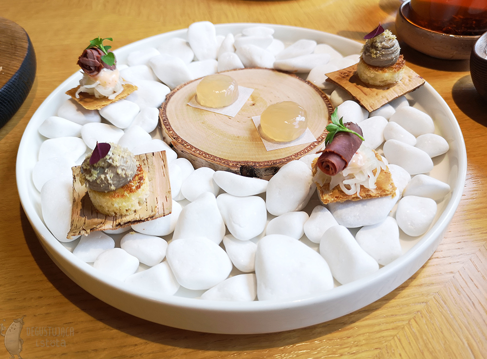  Mini sandwiches and two jelly beans are arranged on a plate filled with white pebbles.