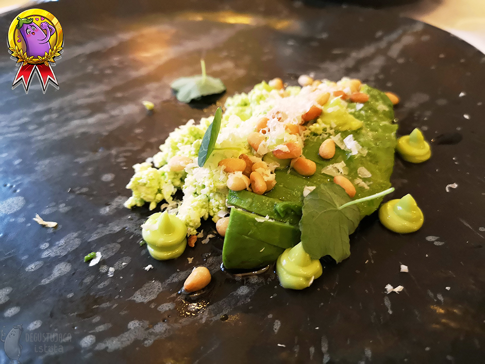 On a black plate sliced ​​avocado and curd are arranged. The whole meal sprinkled with pine nuts and decorated with nasturtium leaves.